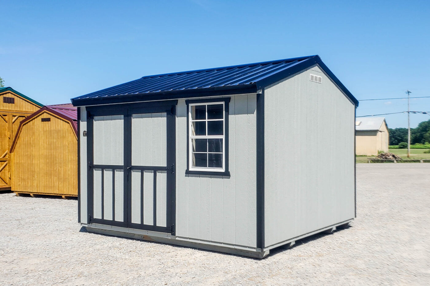 Rear and right-side view of the same 10x12 gray utility shed with black trim and blue metal gable roof, showing a solid wall and a single window.