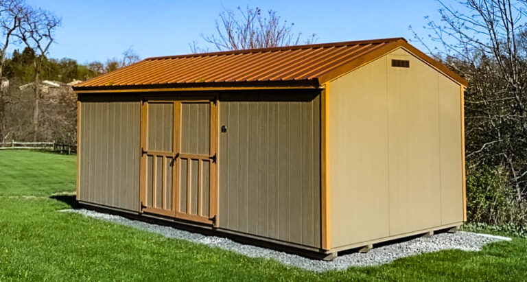 Tan 10x20 utility shed with double doors and a red metal gable roof, sitting on a gravel pad in a grassy backyard with trees in the background.