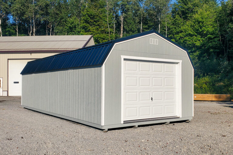Gray lofted garage shed - Gray wood siding with white overhead door beneath dark blue metal roof