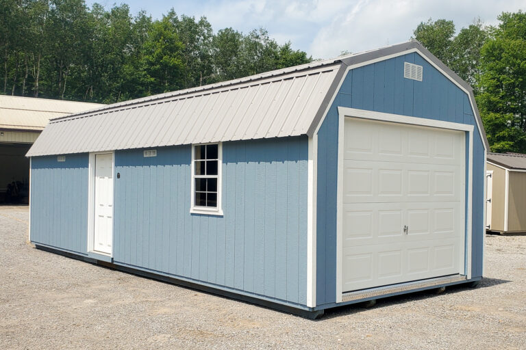 Medium blue Lofted Garage shed - Blue wooden siding with white overhead and side doors and matching window under metal gray lofted roof - green trees in background