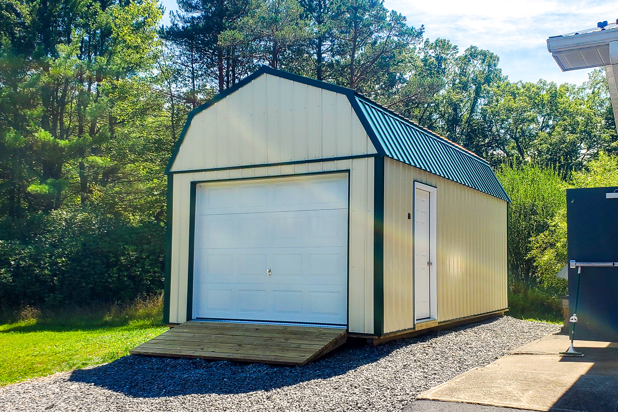 Pale yellow painted lofted metal garage shed with white green-trimmed overhead and side doors under green metal roof