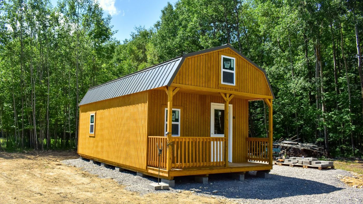 Just-delivered lofted cabin  with wood siding and metal roofing sitting on a gravel pad
